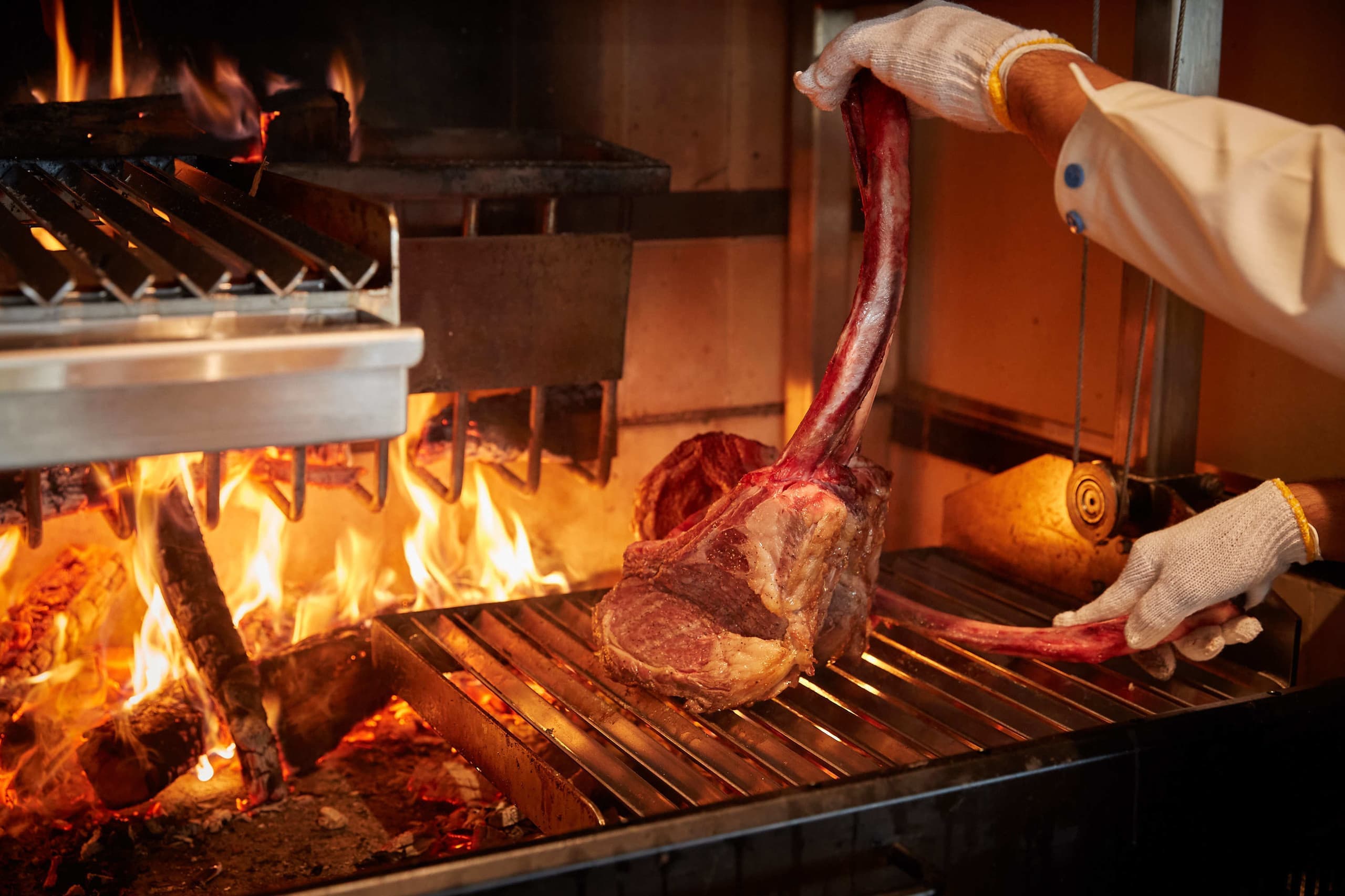 炭火で焼き上げる肉料理の調理シーン写真。炎と焼き色の臨場感を活かしたレストラン向け料理撮影。